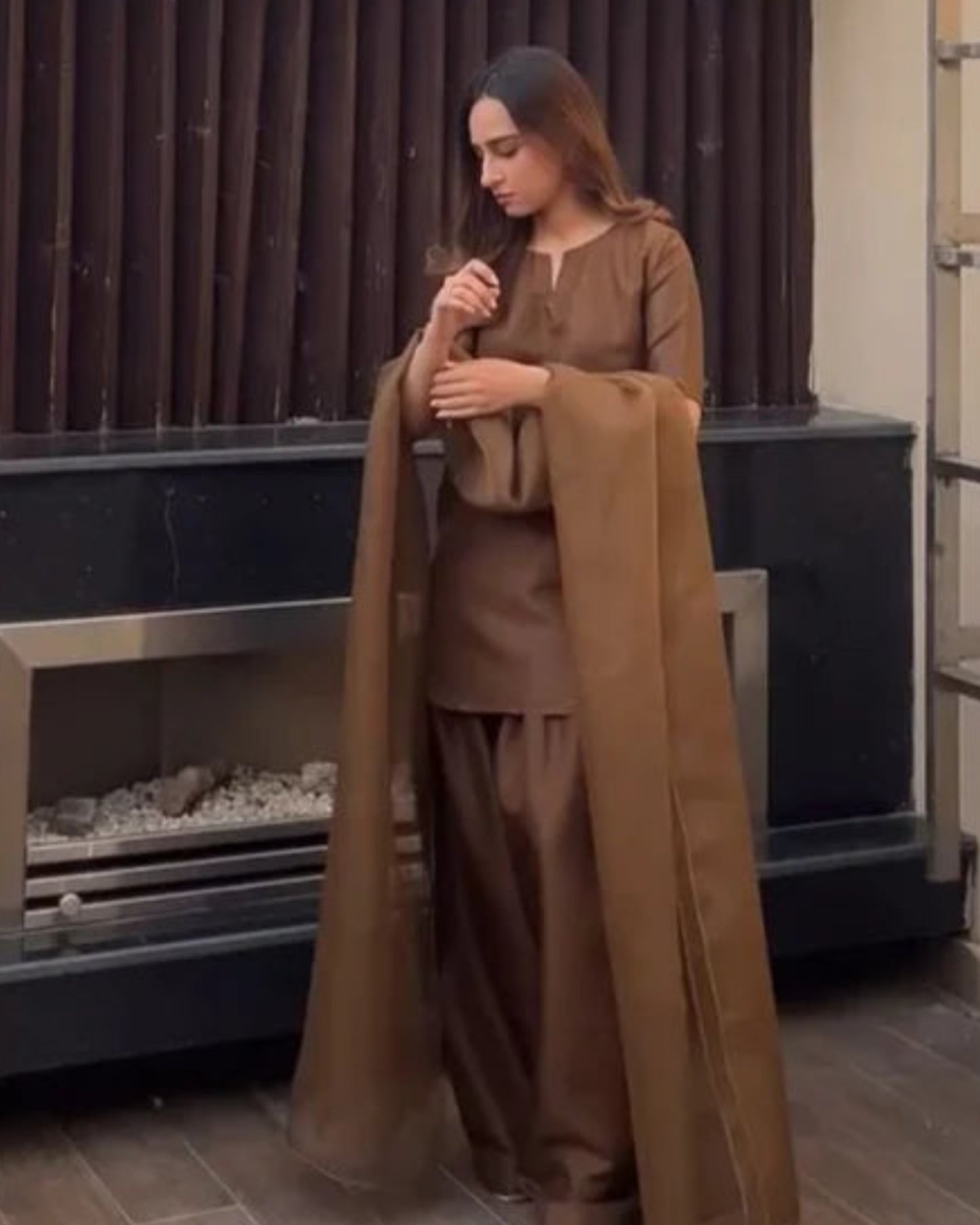 Woman in brown outfit standing by a fireplace outdoors. marhaba pret